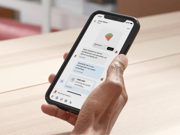 De eigenaar van een bedrijf zit in haar kantoor aan haar bureau en chat via Shopify Inbox op haar mobiele apparaat met een klant. Ze stuurt in de chat een kortingscode door om de verkoop te sluiten.