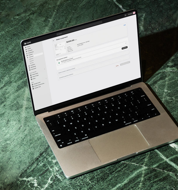 A close-up view of a silver laptop, displaying a payment interface on a marble surface. The screen shows options for importing bills, making a payment, and credit card payments.