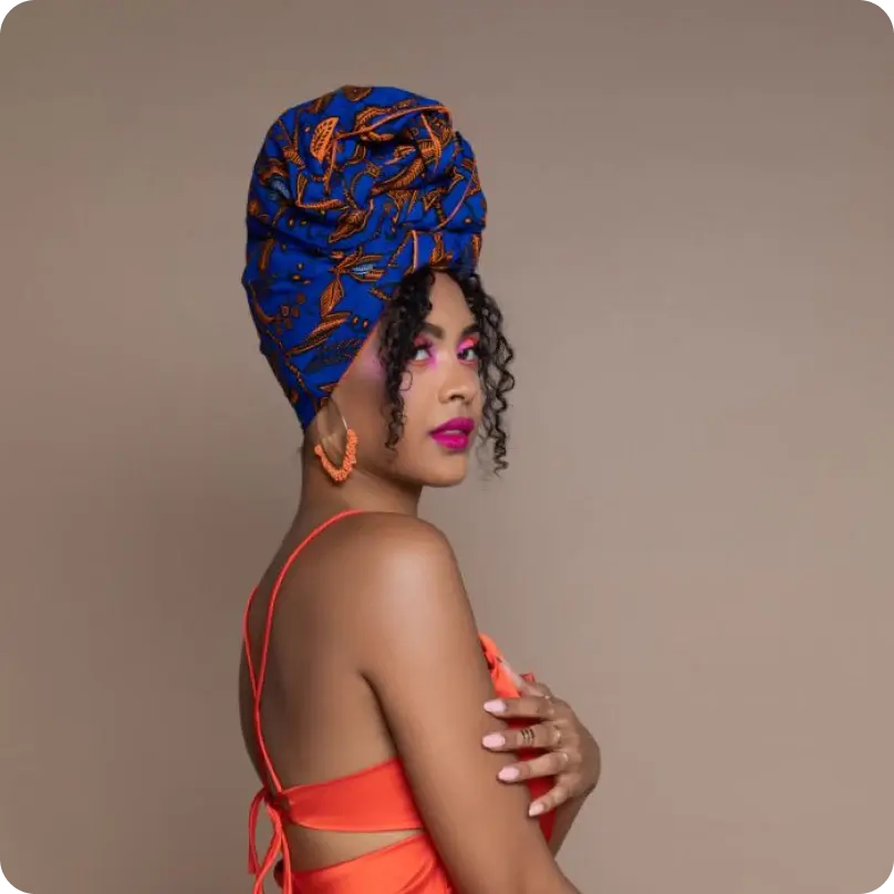 Una mujer con una blusa naranja, un turbante colorido y maquillaje claro