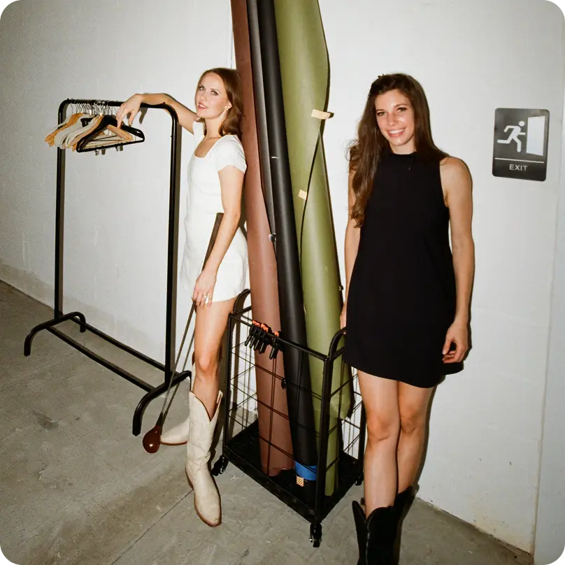 Dos mujeres, una con un vestido de golf blanco y un palo de golf en la mano, la otra con un vestido de golf negro, sonriendo a la cámara