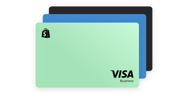 Three stacked business credit cards in varying colors: a mint green card with a Shopify logo and "VISA Business" printed in black, a blue card, and a black card. 