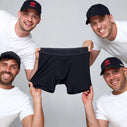 four white men in black hats each holding the corner of a pair of black boxer briefs