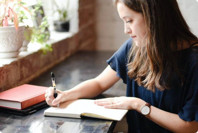 A woman sits at a well-lit desk and writes in her notebook.